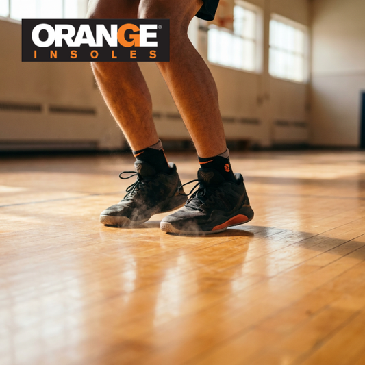 Basketball player landing on a hardwood court in black high-tops — the repeated impact insoles for basketball are meant to absorb